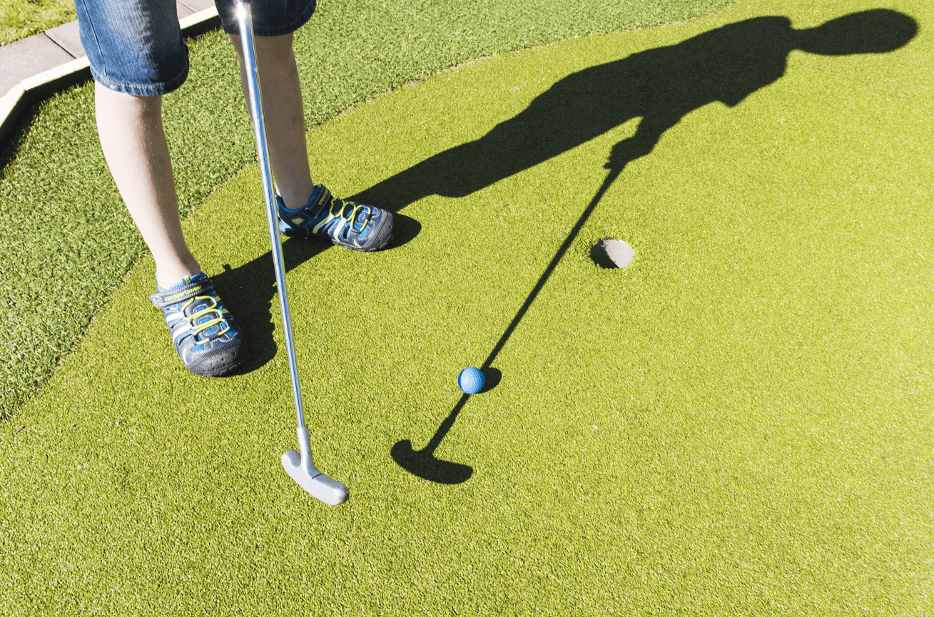 Young boy playing Mapping golf. Looking down at him swinging the putter. Kielder Waterside